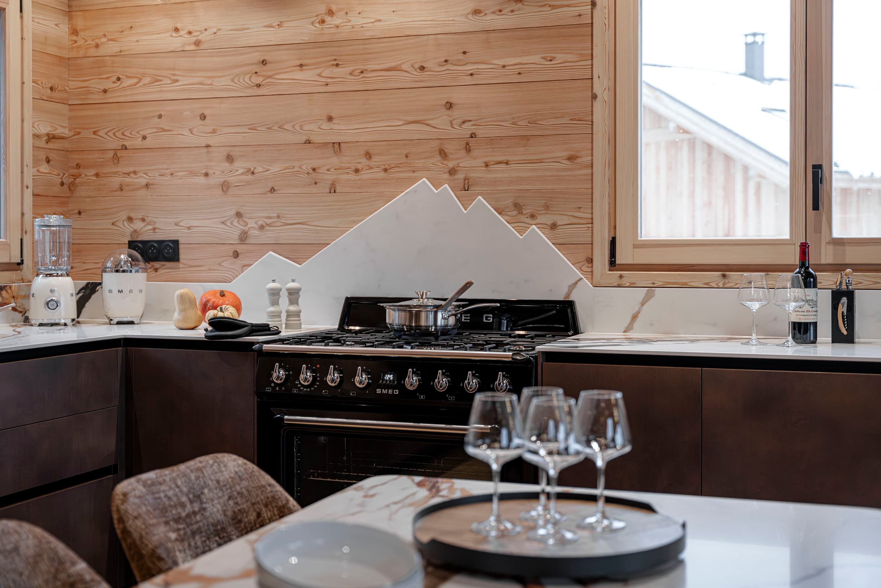 Cuisine vue d'angle avec deux fenêtres, piano Smeg noir et plan de travail en marbre