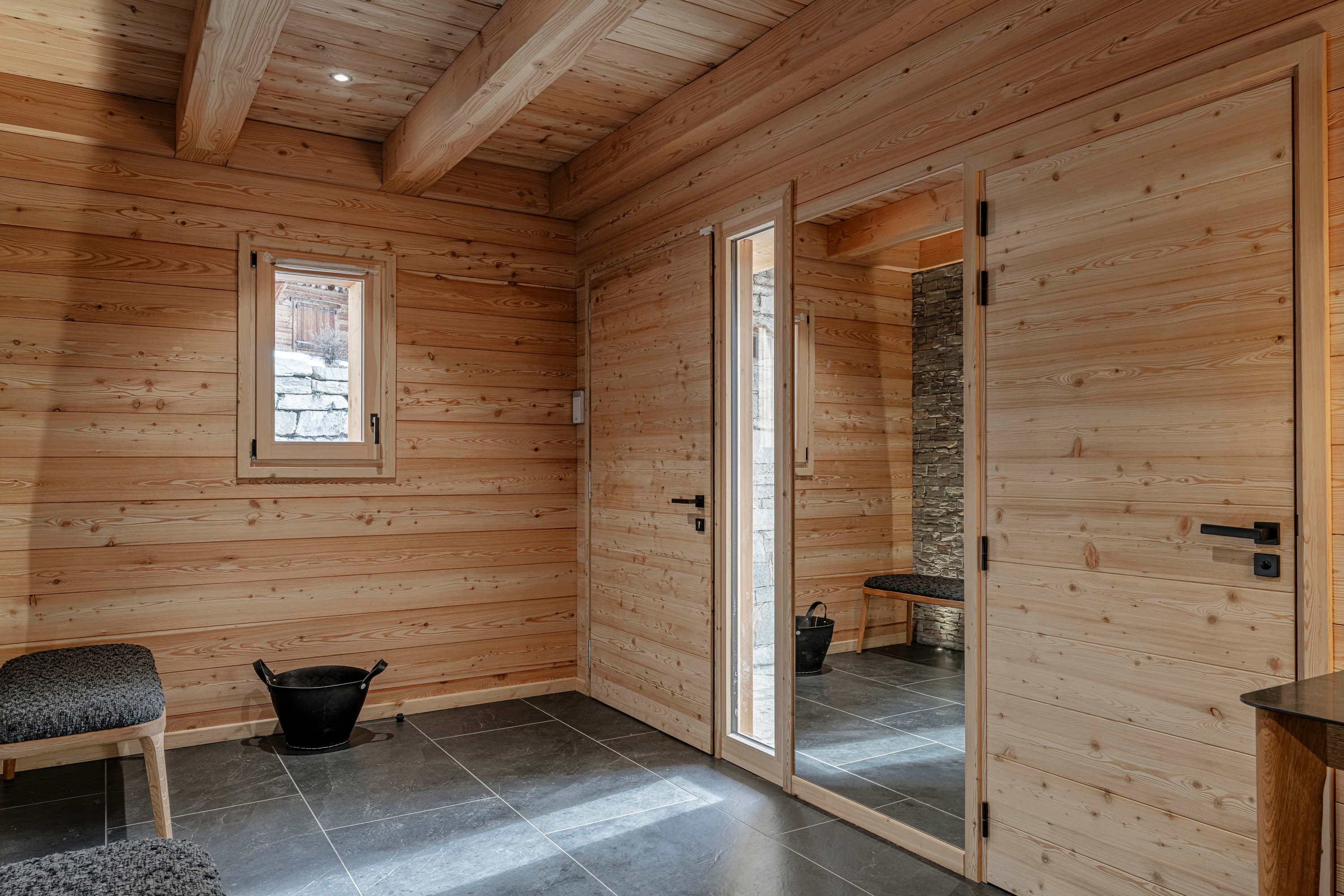 Hall d'entrée en bois clair avec porte vitrée, banc et sol en ardoise