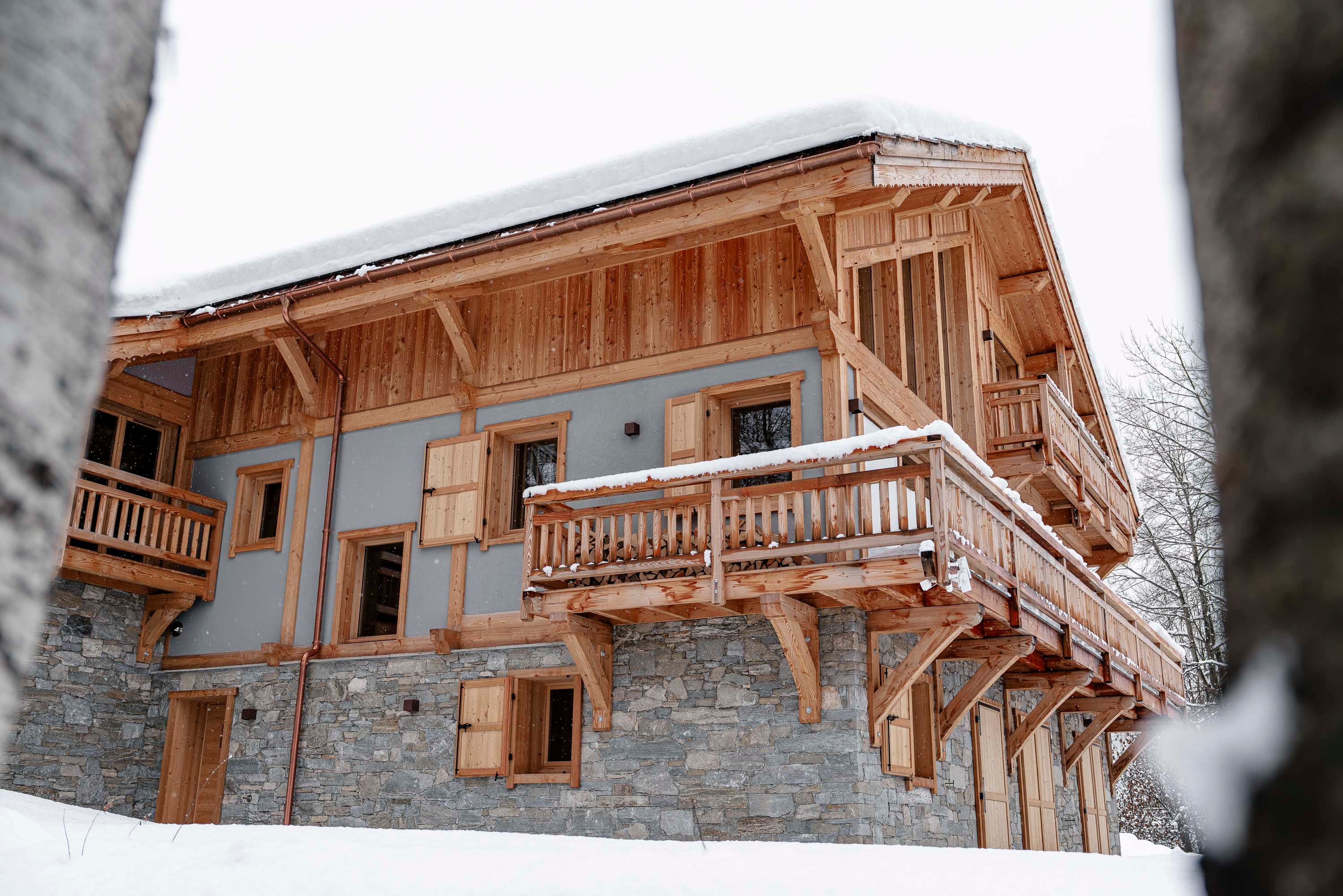 Balcon et façade latérale du chalet entre les troncs de bouleaux sous la neige