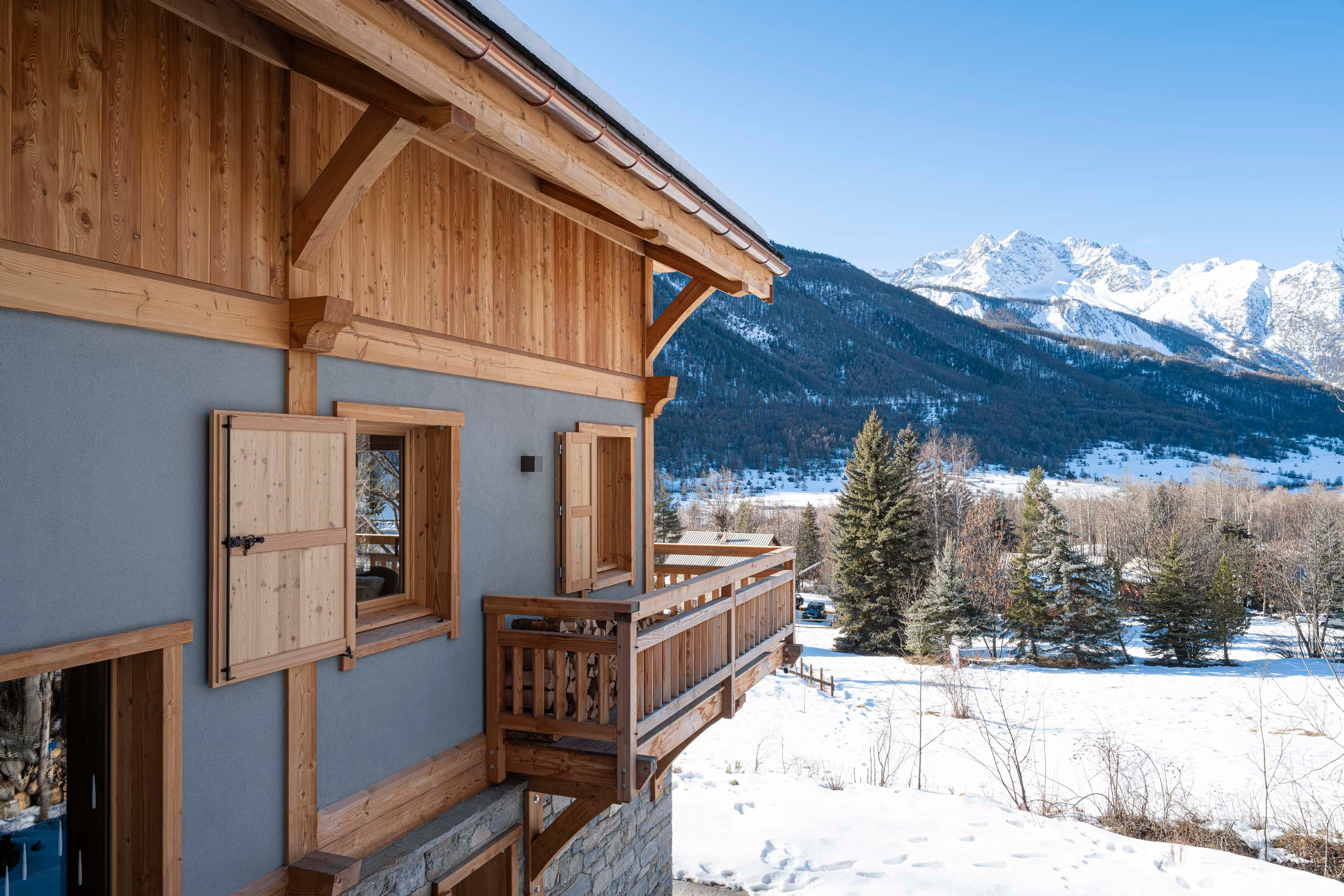 Façade latérale du chalet avec balcon et vue sur la vallée du Monêtier et les montagnes
