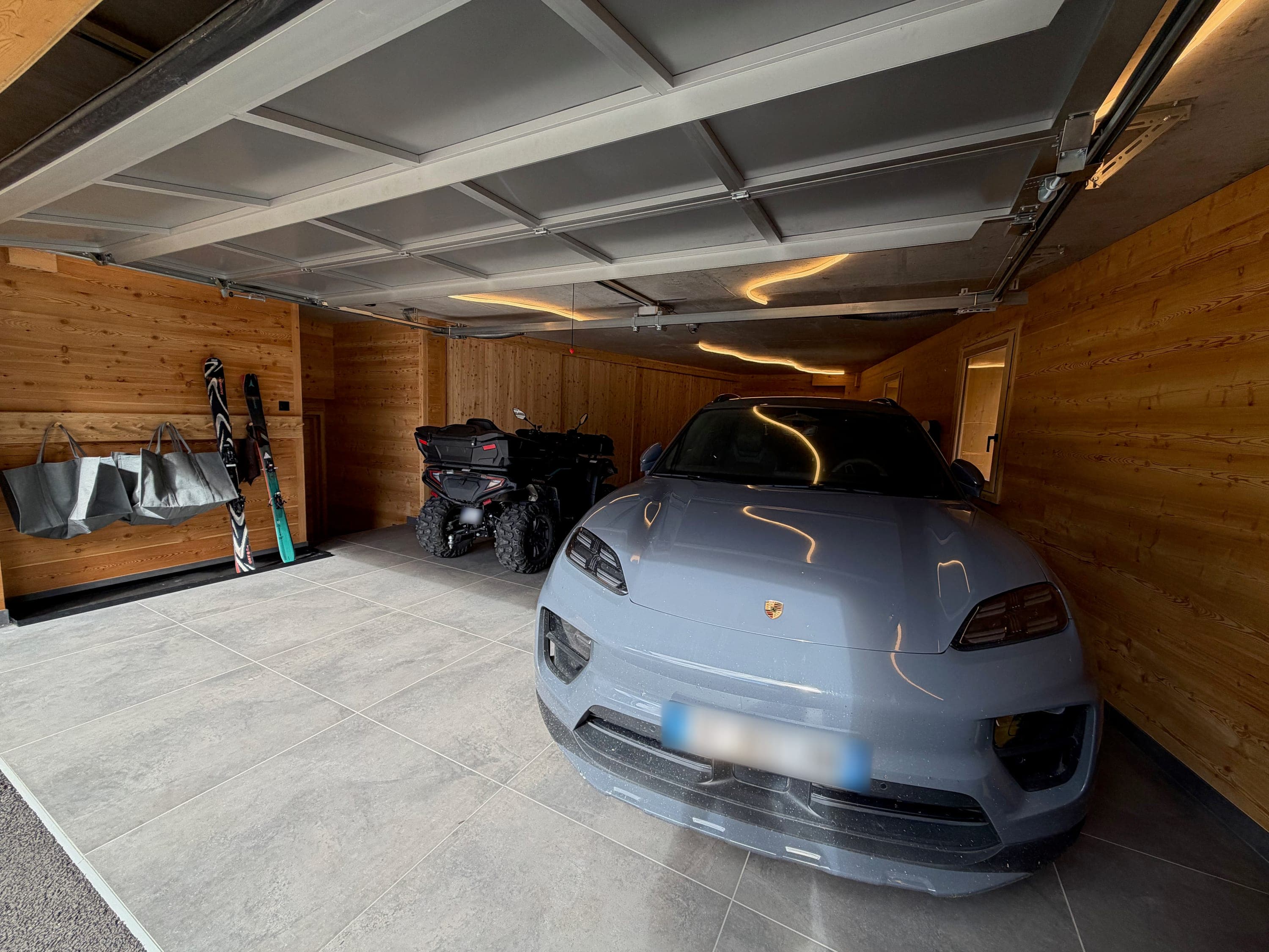 Garage habillé de bois avec une voiture électrique et un quad stationnés, skis rangés au mur