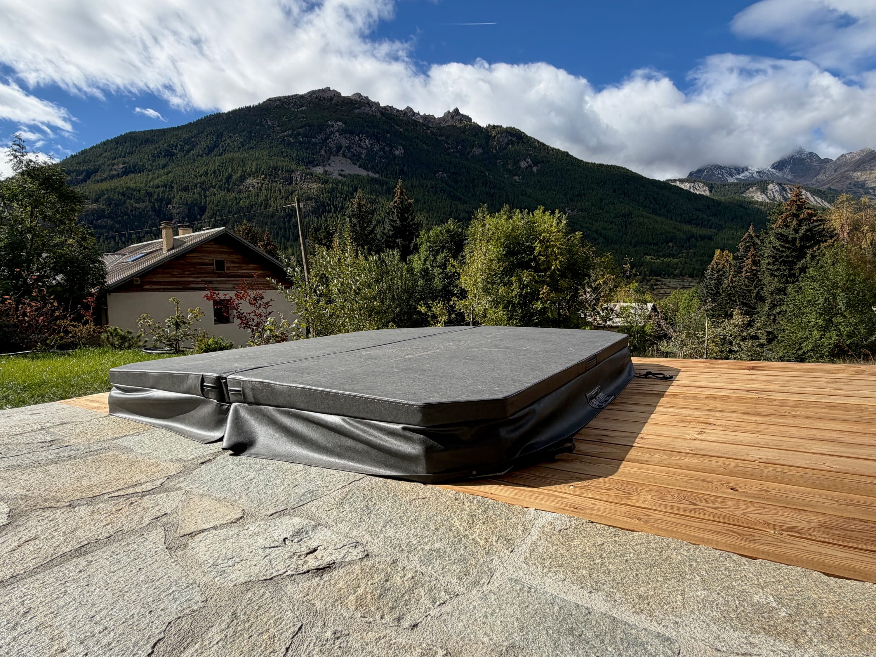 Jacuzzi sous sa couverture, entre la terrasse en pierre et le deck en bois, face à la montagne