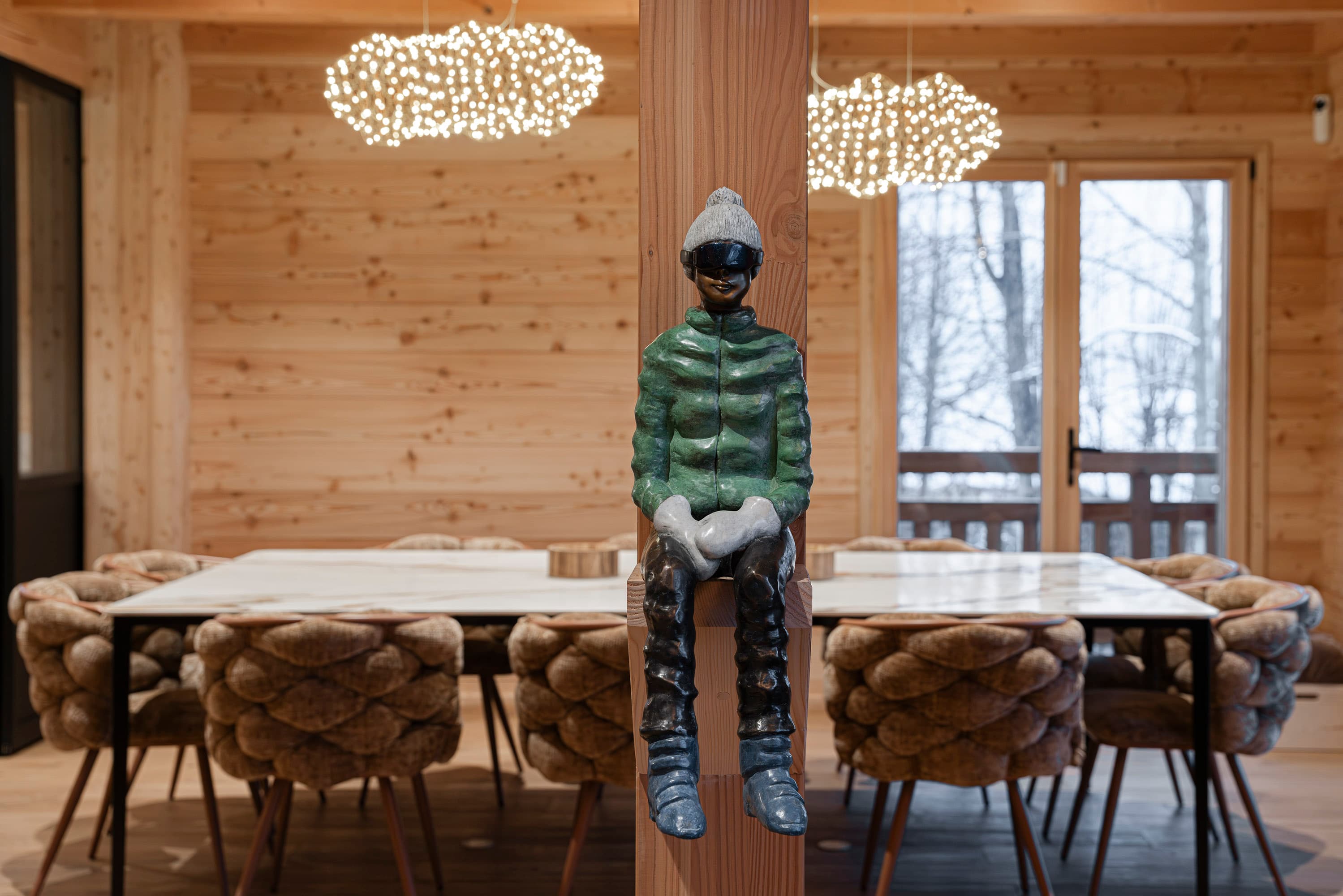 Sculpture de skieur en bronze assis sur une poutre devant la table et les suspensions nuage