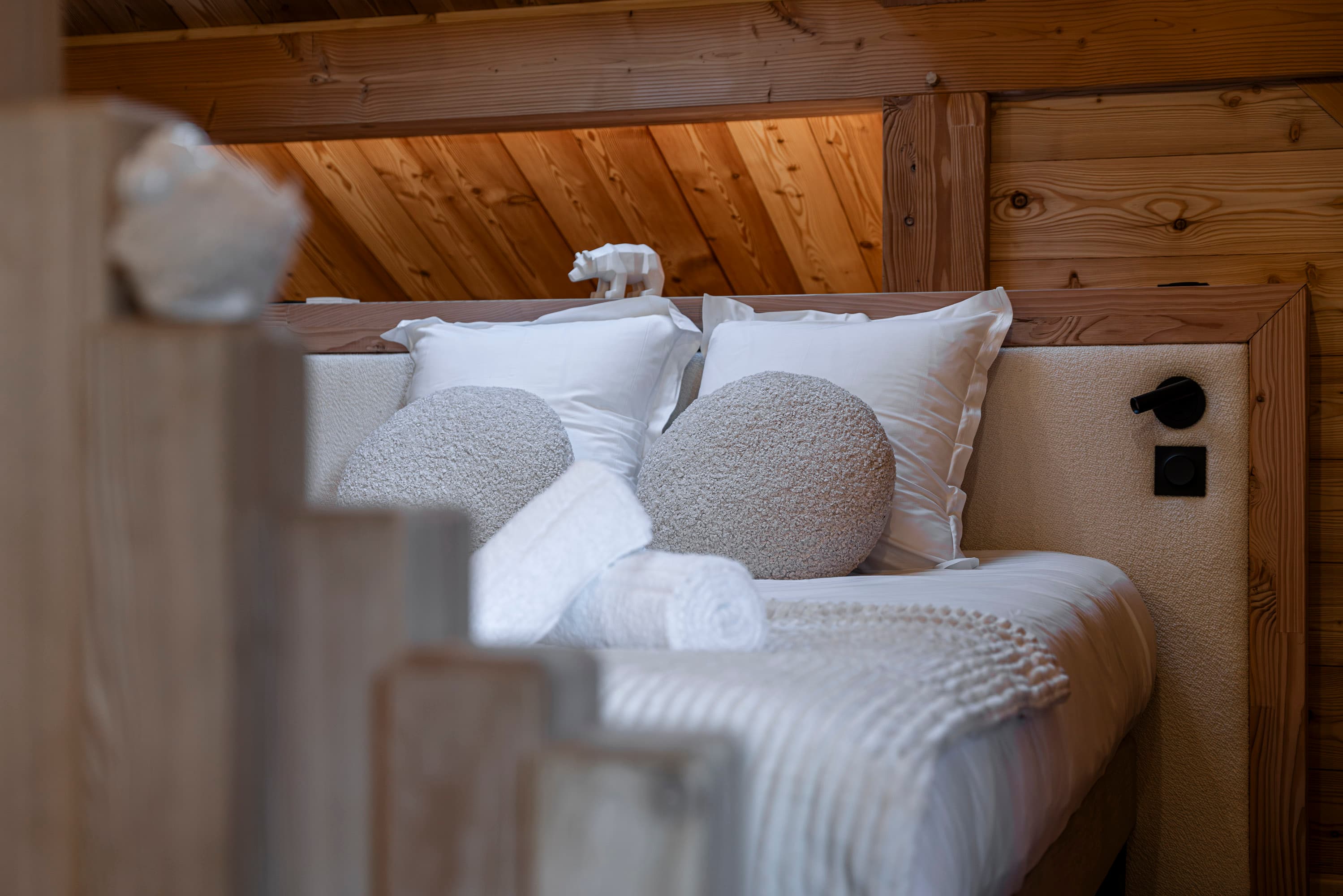 Détail du lit avec coussins ronds bouclés, figurine ours polaire et serviettes roulées